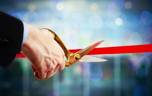 Businessman cutting red ribbon with pair of scissors close up